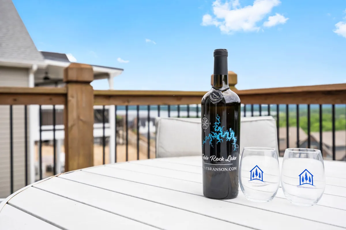 A close-up of a table set with a wine bottle and two glasses is positioned on an outdoor deck, overlooking a scenic view. The setting evokes moments of relaxation, such as sipping evening cocktails or enjoying a celebratory toast while taking in the natural surroundings. The image highlights both the social and serene aspects of the deck experience.