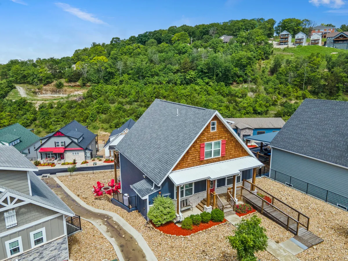 A charming exterior view of Hawthorn House, featuring vibrant red patriotic accents, a landscaped yard, and a welcoming porch amid lush greenery. The scene includes neighboring homes, indicating the sense of community and festive curb appeal.