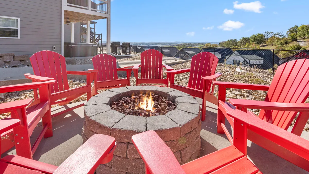 A relaxed outdoor setting with a fire pit circled by red chairs, set against a scenic backdrop. The setup is ideal for group gatherings, storytelling, and making s'mores under the stars.