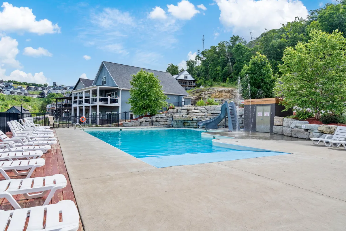 A vibrant exterior shot featuring a large swimming pool surrounded by lush greenery, with a slide extending into the water. Lounge chairs are arranged along the poolside, suggesting a space perfect for families and gatherings. The area has a lively, joyful atmosphere, ideal for both children and adults to have fun and relax.