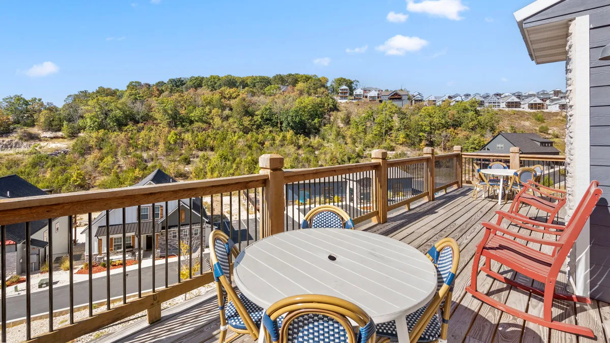 This exterior shot focuses on a spacious wooden deck furnished with outdoor seating, providing panoramic views of rolling hills and surrounding homes. The setting sun casts a warm glow, creating an inviting scene ideal for both relaxation and social events. The deck blends seamlessly with its natural surroundings, emphasizing the extension of indoor comfort into the outdoors.