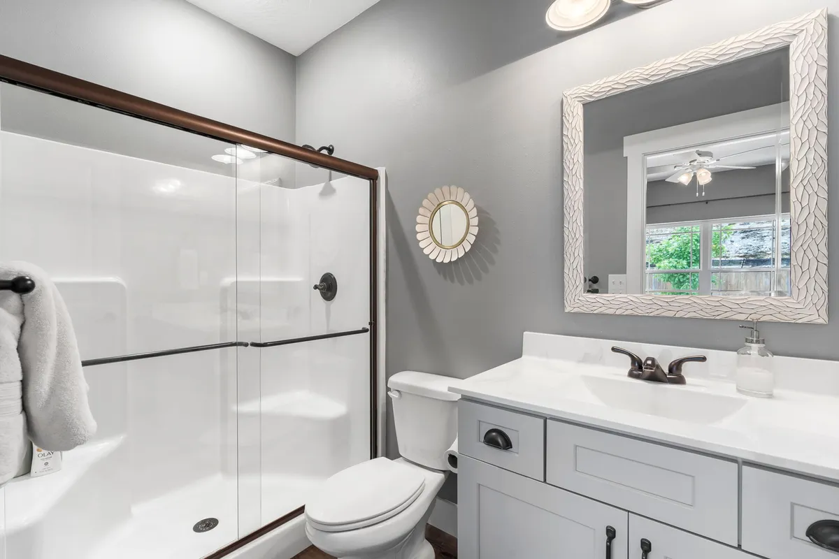 A pristine bathroom featuring a vanity with sink, bright mirror, and a spacious shower area. The design is clean and calming, ideal for moments of relaxation and self-care.