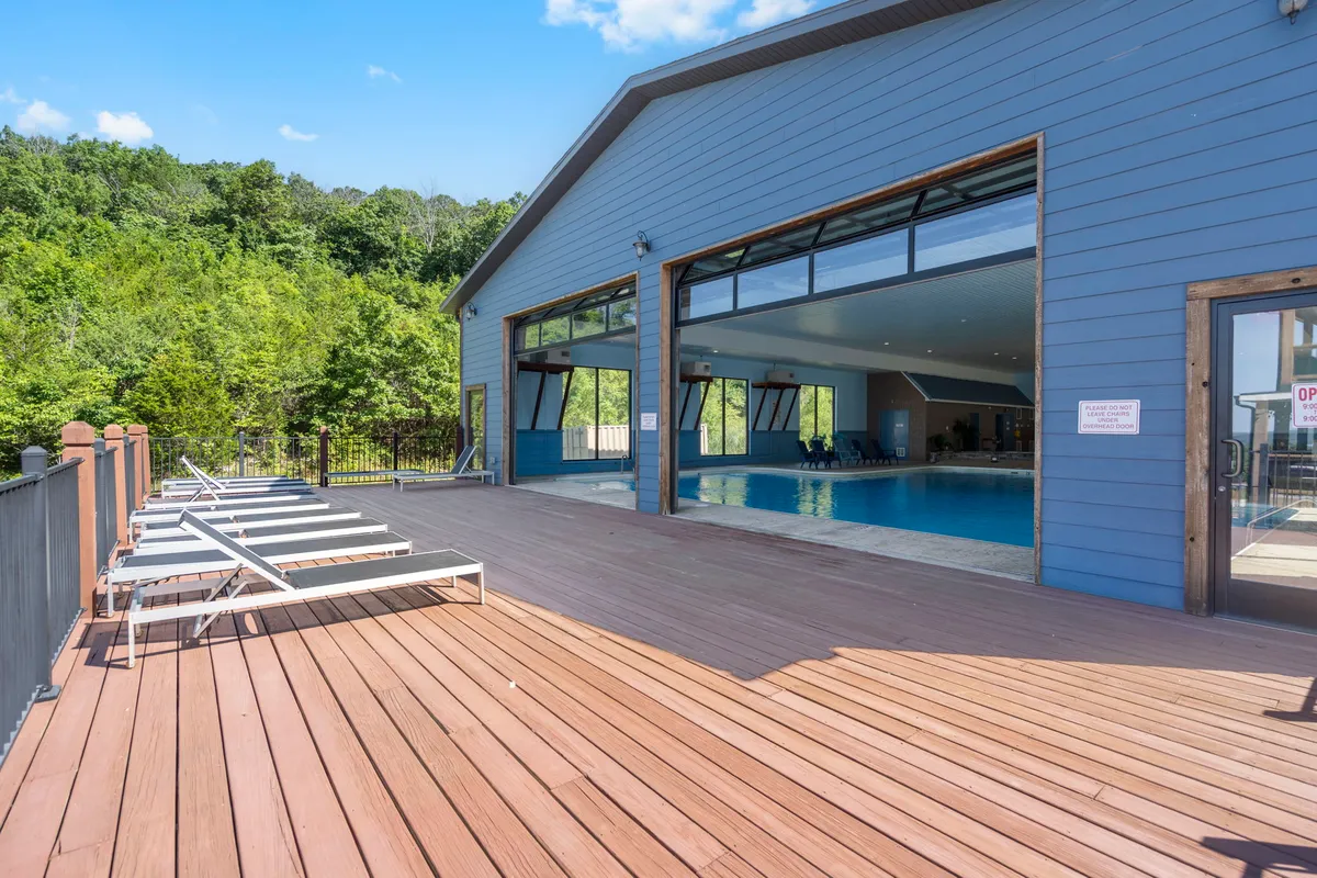 A vibrant exterior view of the outdoor pool area, featuring a spacious deck, large open windows overlooking the water, and lush greenery surrounding the space. The pool is the focal point, with areas for swimming, sunbathing, and socializing, all set against a backdrop of natural beauty.