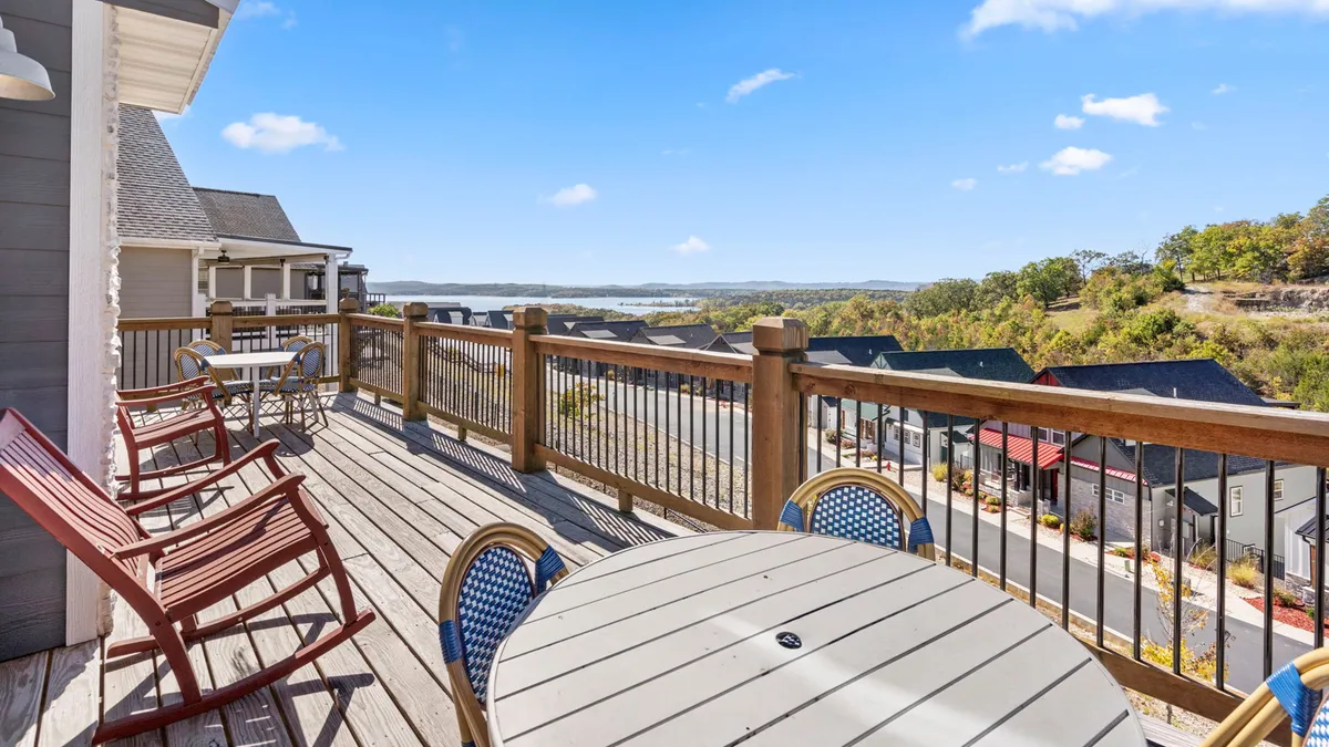 This image showcases an inviting outdoor seating area on a wooden deck, with comfortable chairs overlooking a tranquil landscape. The wooden railing frames the view, and the scene captures the peacefulness of being outdoors, perfect for relaxation or social gatherings. The angle emphasizes the deck as an extension of the indoor living space, blending comfort with the beauty of nature.
