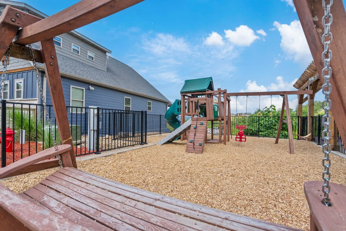 A cheerful outdoor playground scene featuring a swing set and play structure set in a sand area. The space is designed for children’s enjoyment and family gatherings, emphasizing safe, active play in a welcoming environment.